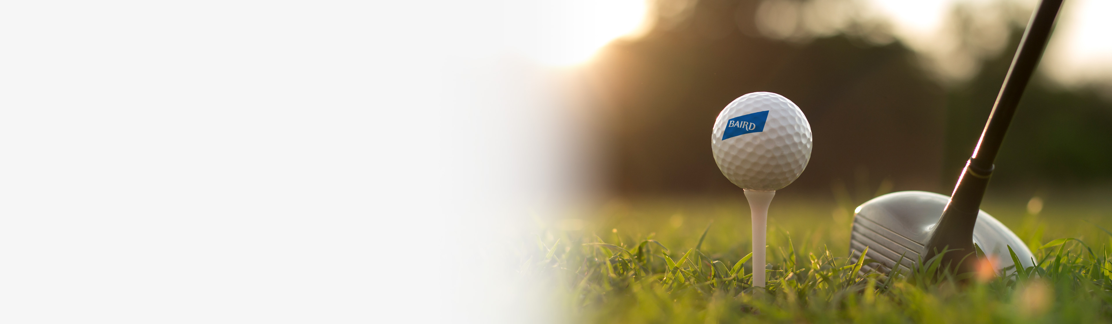Baird branded golf ball on a tee accompanied by a golf club.