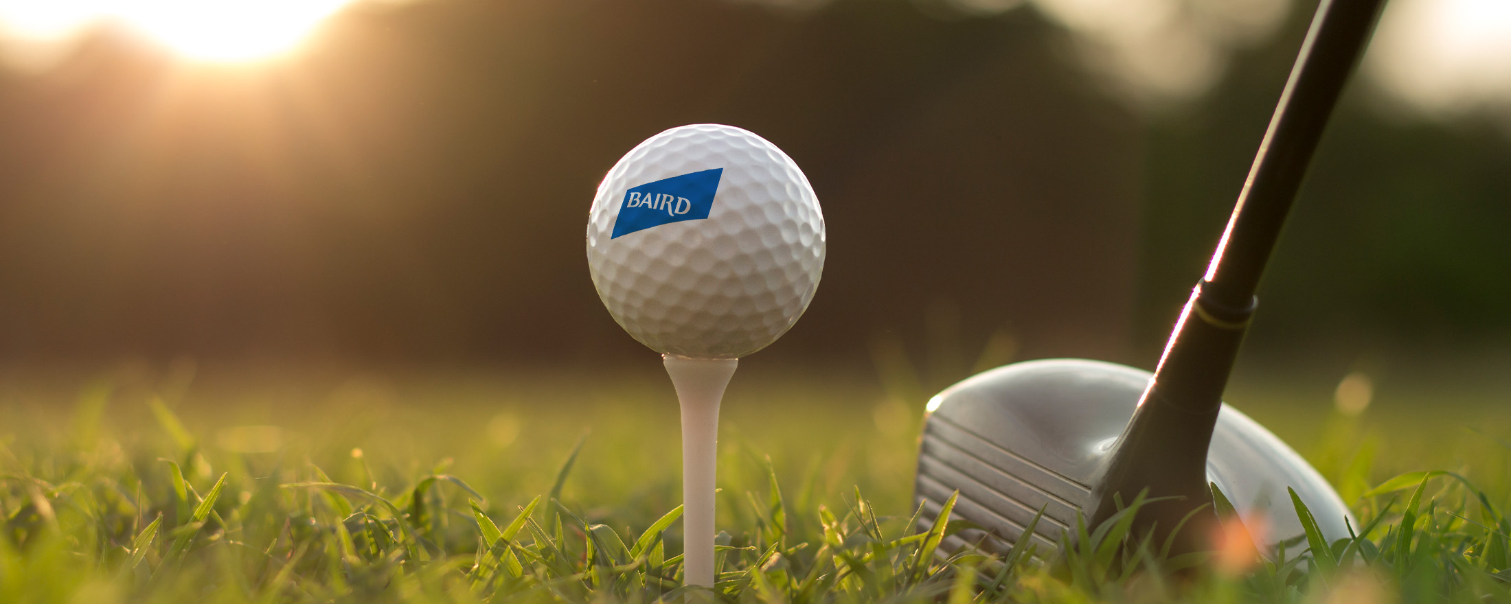Baird branded golf ball on a tee accompanied by a golf club.